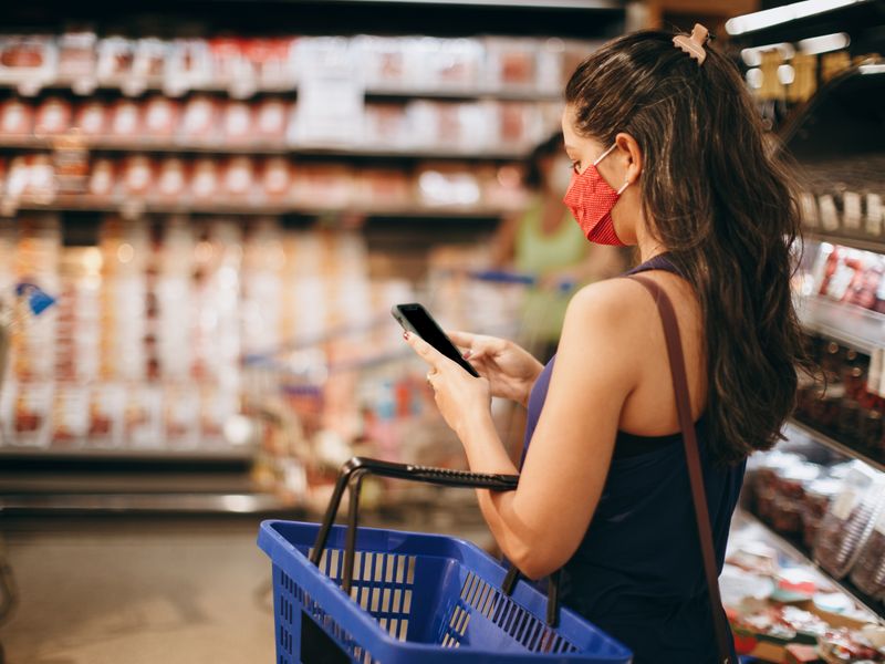 Woman checking unit prices on her phone in a grocery aisle
