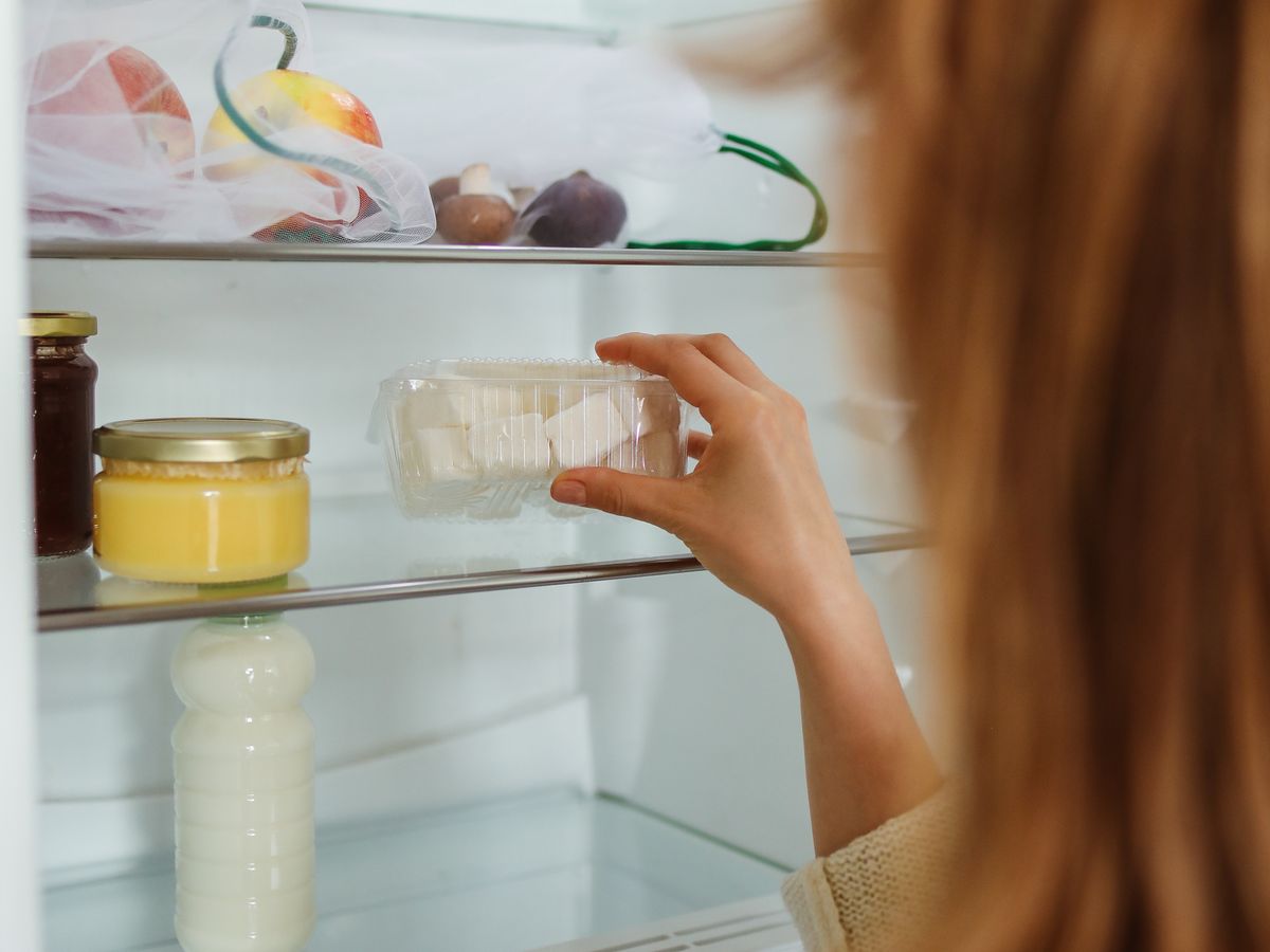 Woman reaching into a refrigerator for a stored food container, illustrating safe storage while you plan a week of meals for one