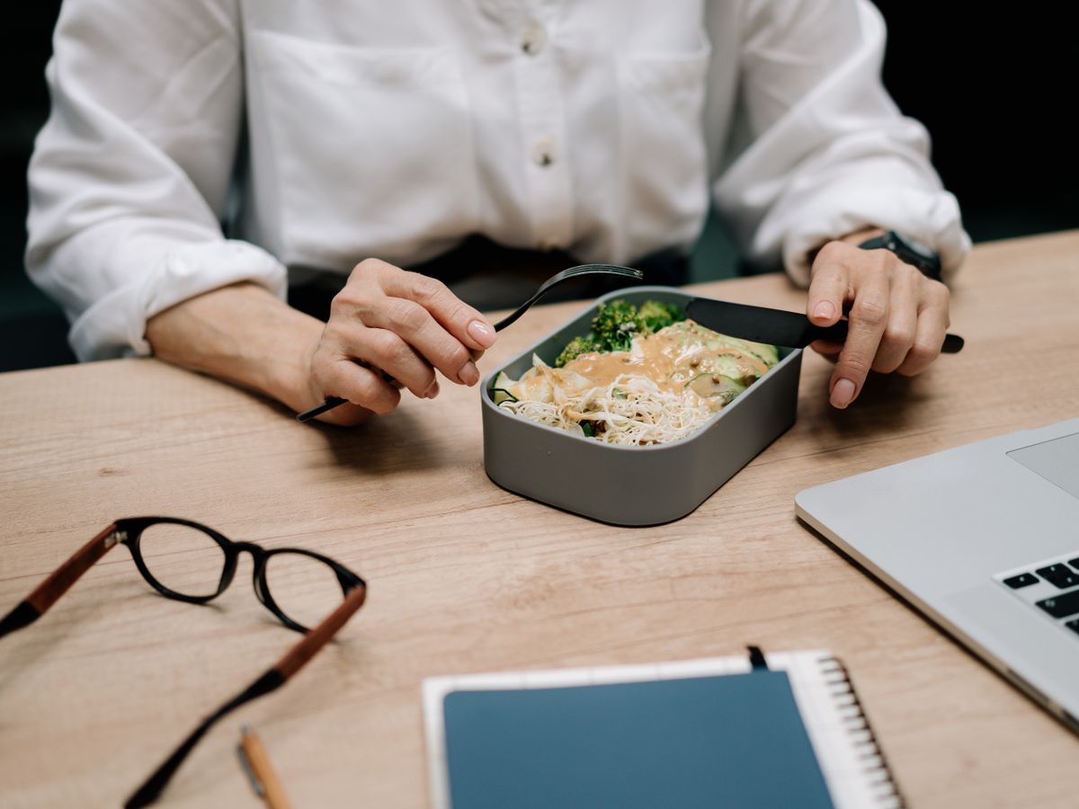 Person eating leftovers from an easy dinner for one out of a lunch container at a desk